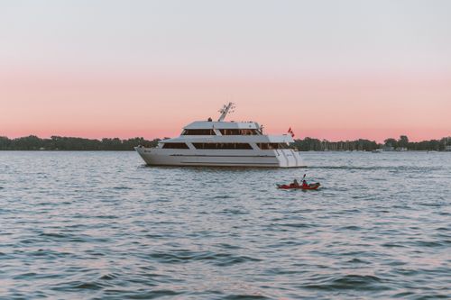 Free A serene scene of a yacht during sunset, accompanied by two kayakers enjoying the tranquil water. Stock Photo
