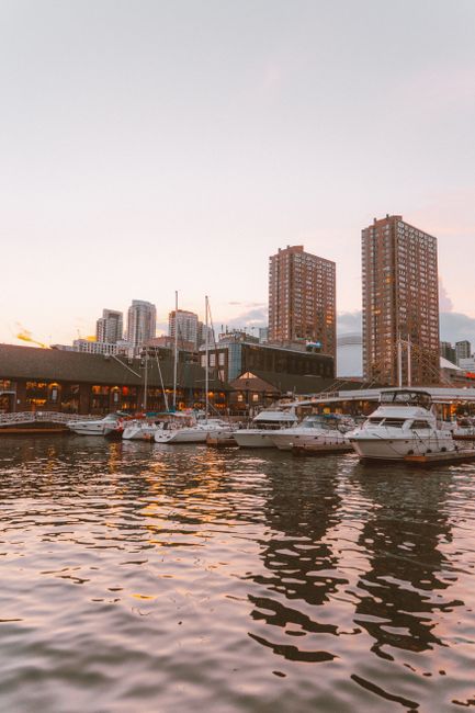 Beautiful marina scene with boats and city skyline during sunset, reflecting tranquil waterfront ambiance.