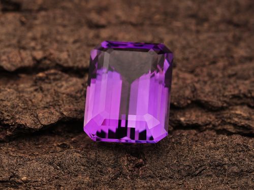 Free Close-up of a radiant purple amethyst gemstone placed on a rugged textured surface, highlighting its clarity and cut. Stock Photo