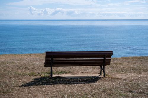 Free A tranquil scene of a bench facing the vast, calm ocean, perfect for contemplation. Stock Photo