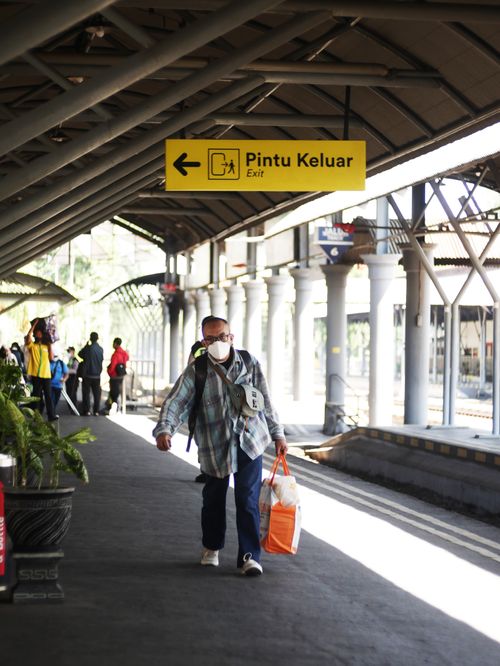 Free A man wearing a mask walks with luggage under an exit sign at Surabaya train station. Stock Photo
