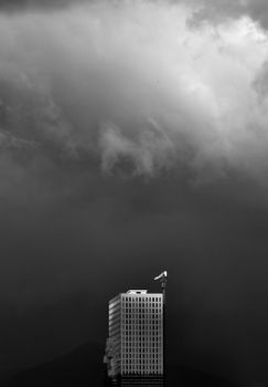 A solitary building stands tall against a dramatic, cloud-filled sky in monochrome.