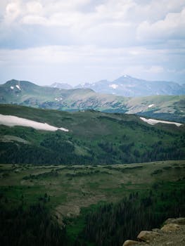 Lush green hills and distant snow-capped mountains under a cloudy sky, creating a tranquil scene.