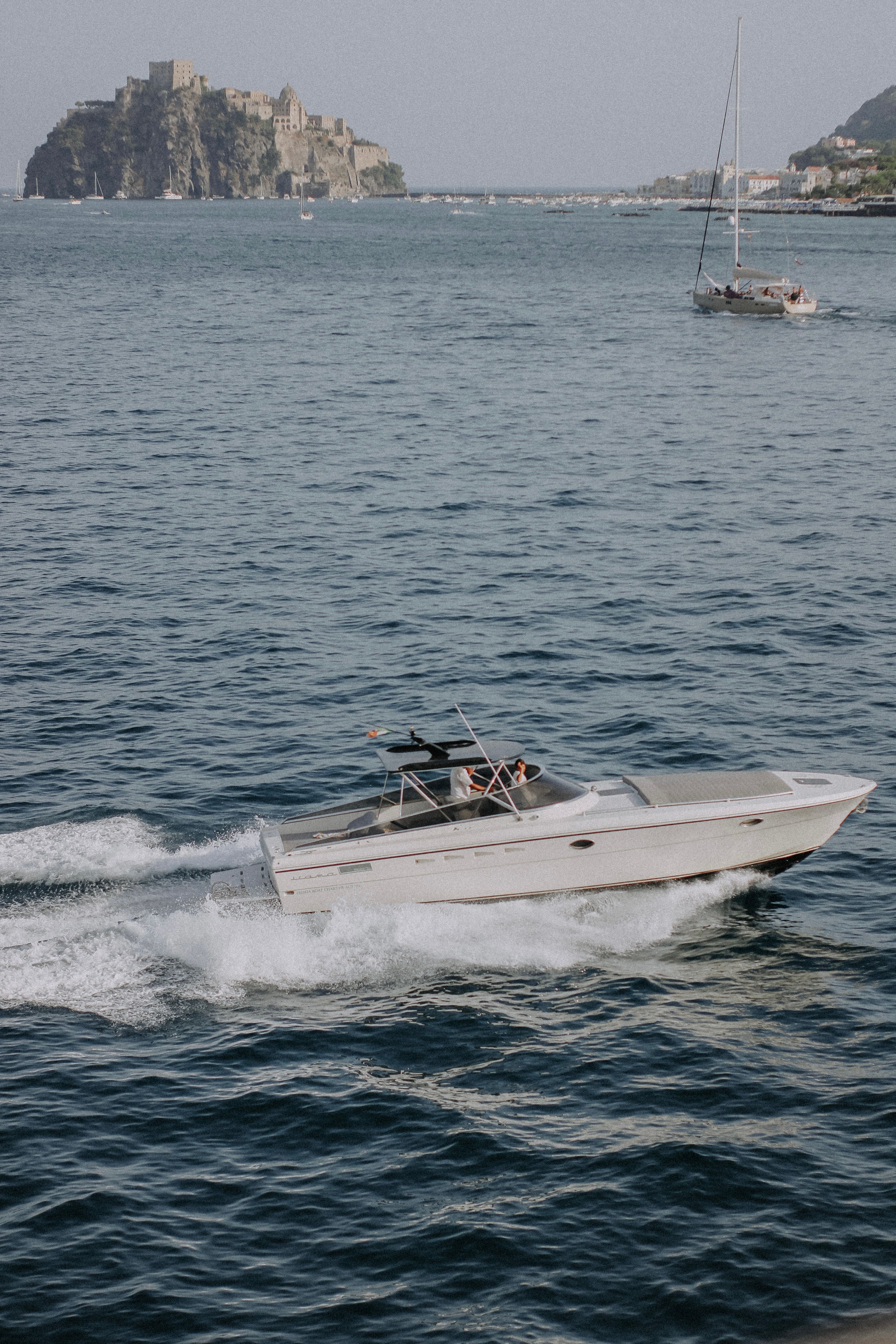 A motorboat speeds by a distant island castle under a clear sky, creating a dynamic scene on the water.