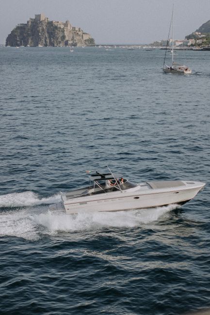 A motorboat speeds by a distant island castle under a clear sky, creating a dynamic scene on the water.