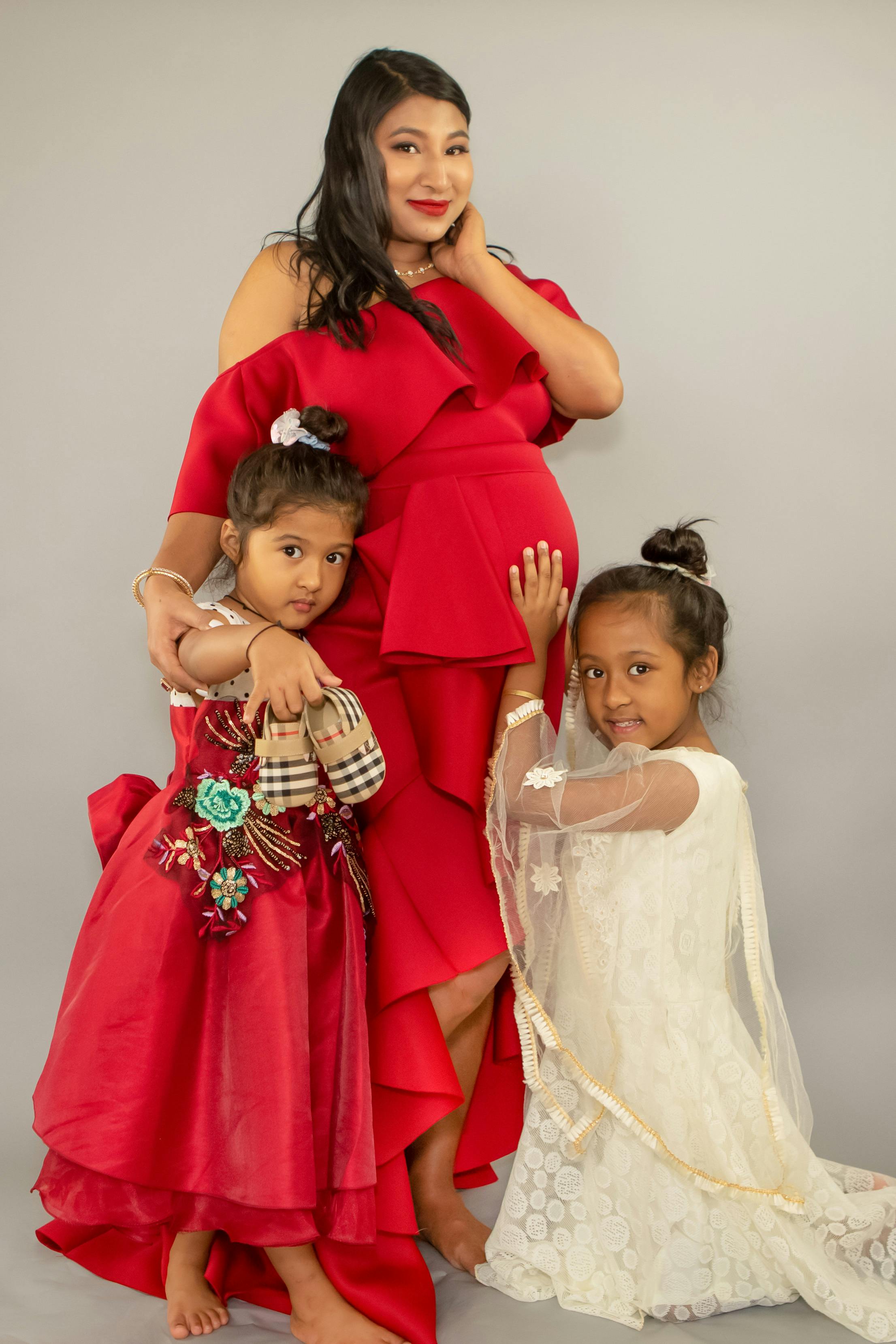 girls in red and white dresses beside their pregnant mother in red dress