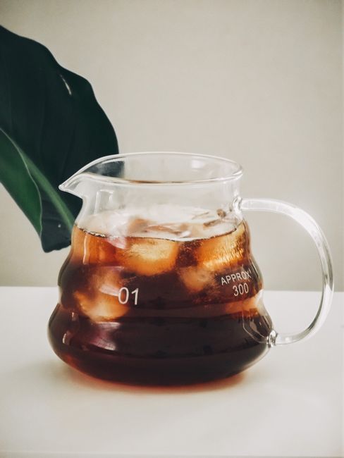 A glass pitcher of amber cold brew tea with loose tea leaves settled at the bottom and a filled glass of iced tea beside it.