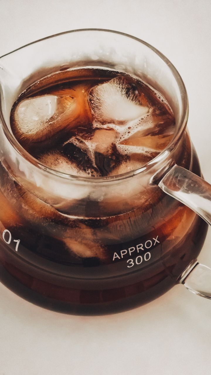 clear glass cold brew carafe with a lid sitting on a kitchen counter next to coffee mugs
