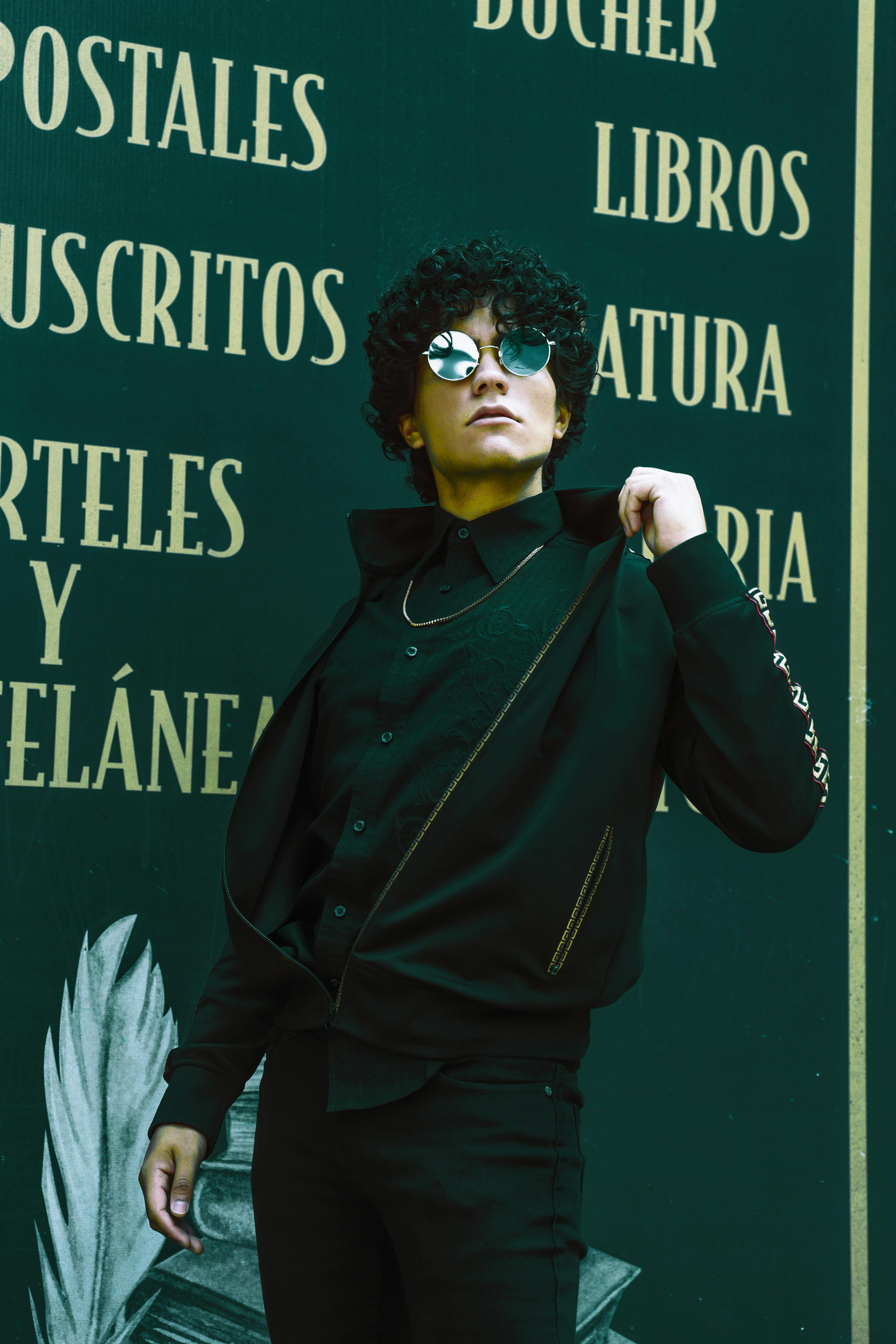 Confident man in black clothing and sunglasses poses with stylish flair