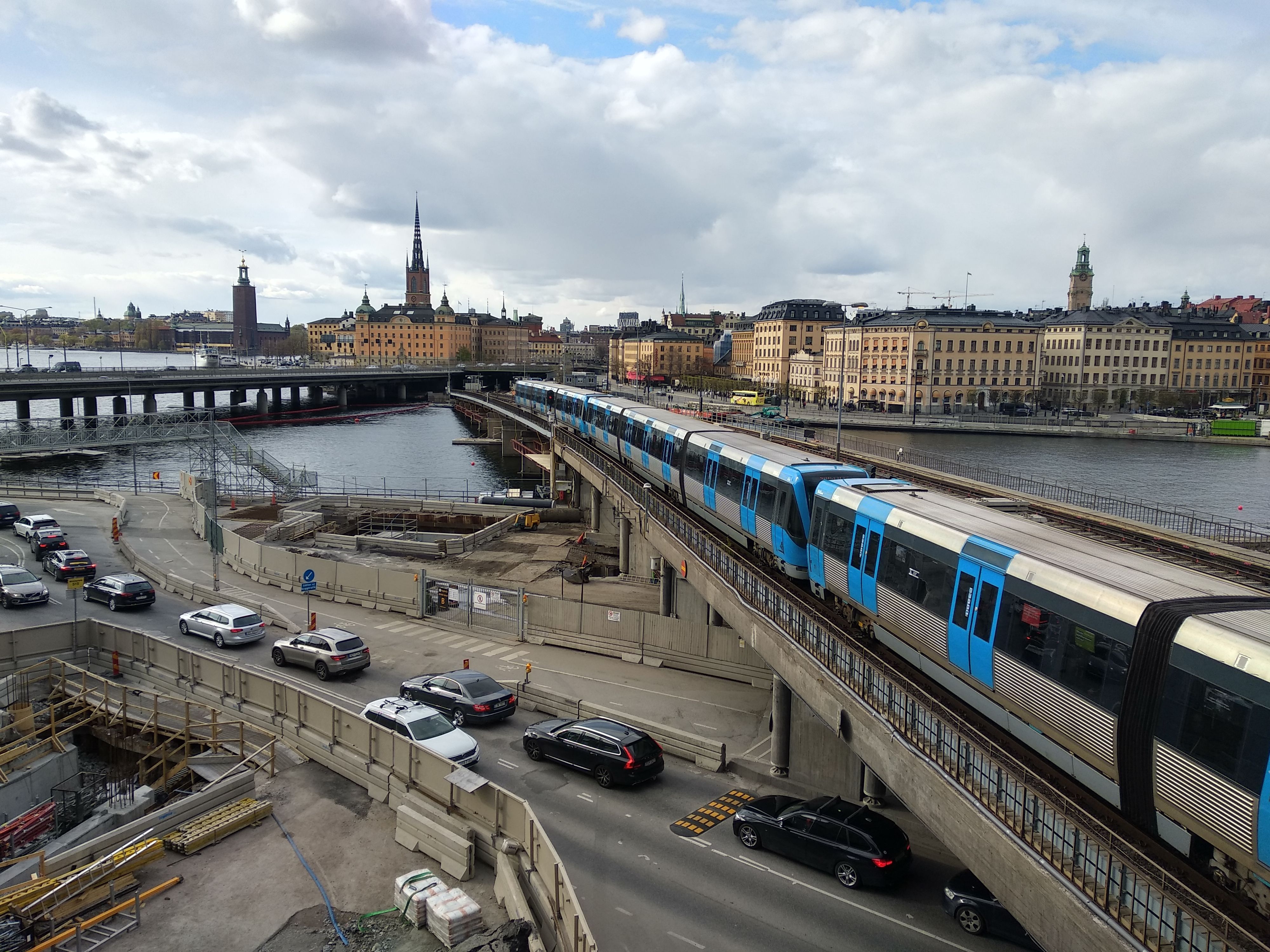 A busy intersection in Stockholm featuring a train, cars, and historic architecture.