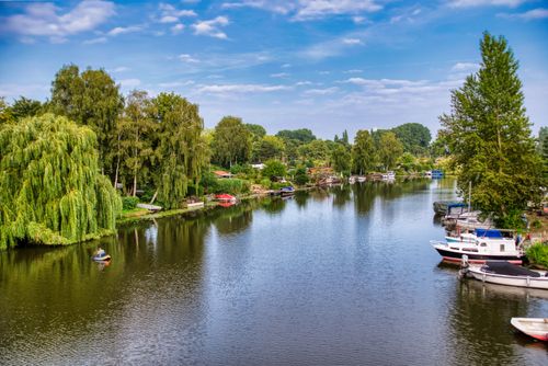 Free A tranquil river scene with boats and lush trees reflecting on water under a clear blue sky. Stock Photo