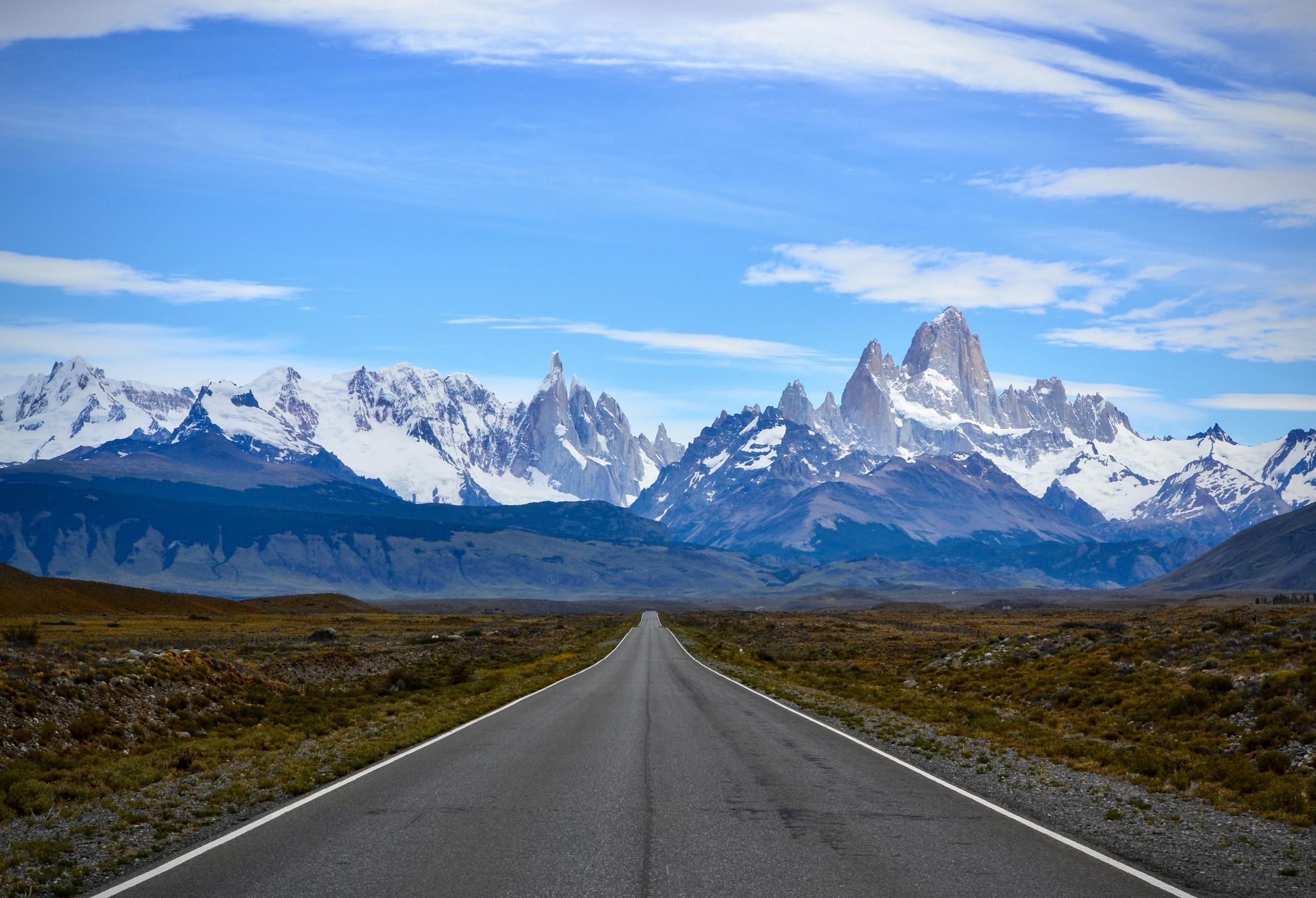 Discover the breathtaking view of Mount Fitz Roy with a clear blue sky and endless road leading to the mountains.