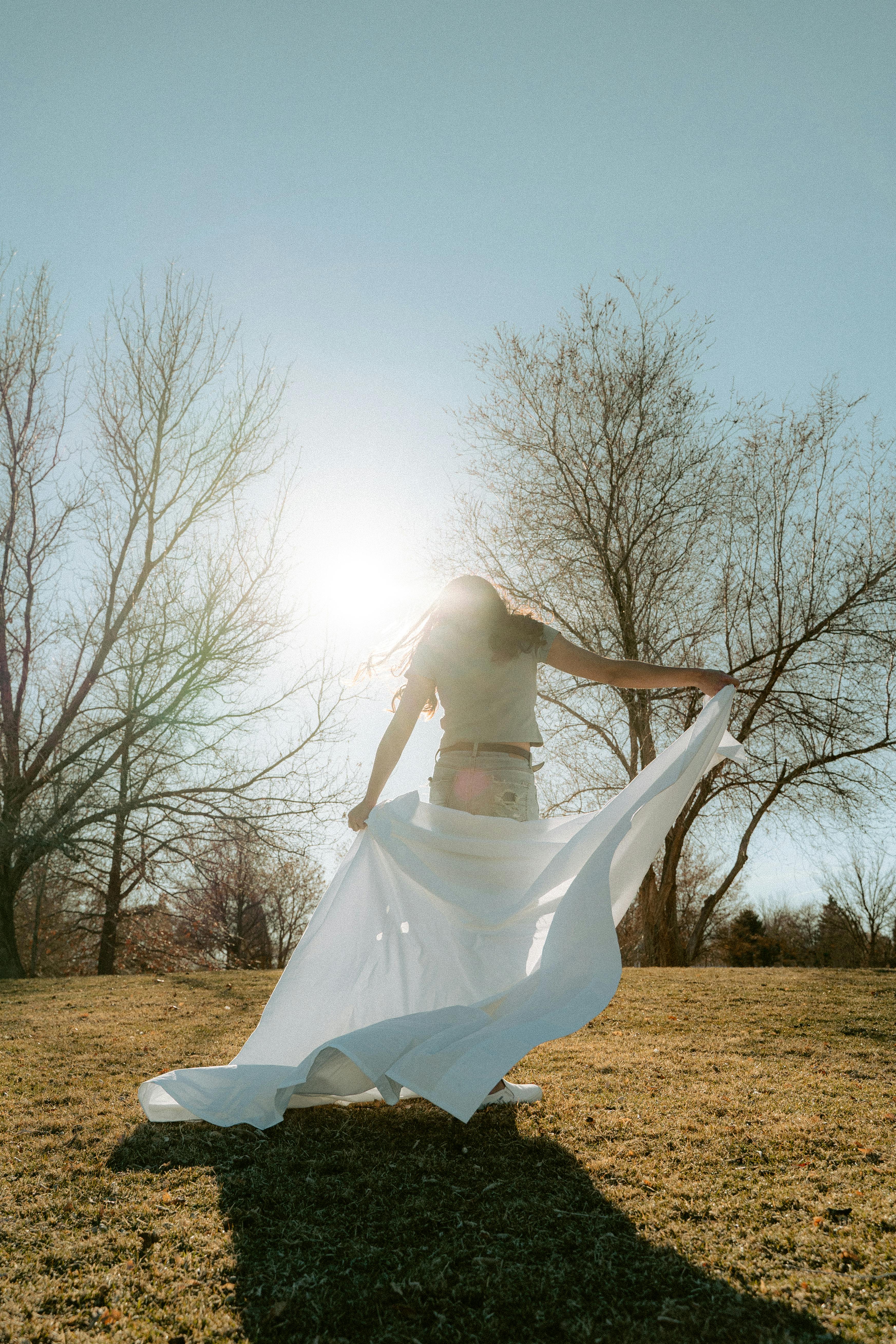 Woman standing in a sunny grassland, holding white cloth and enjoying nature.