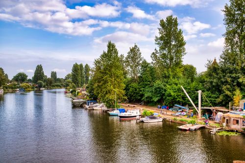 Free Tranquil rural riverscape with boats docked along a tree-lined shore under a blue sky. Stock Photo