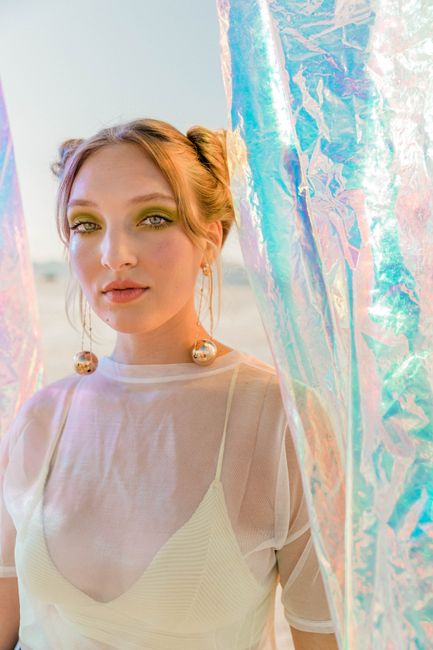 Stunning portrait of a young woman in iridescent light with sheer blouse and bold makeup.