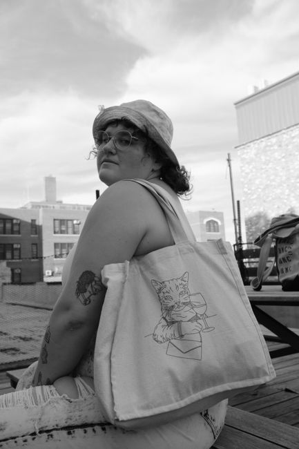 A fashionable woman with glasses and tattoos carrying a cute tote bag in a city environment.
