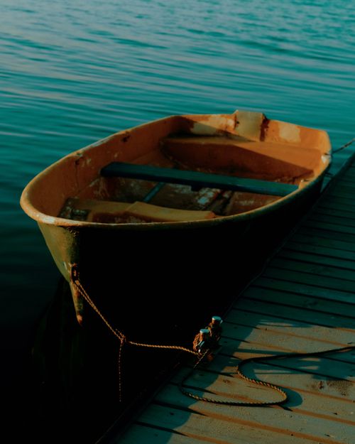 Free A tranquil scene of a wooden rowboat tied to a pier at sunset over calm waters. Stock Photo