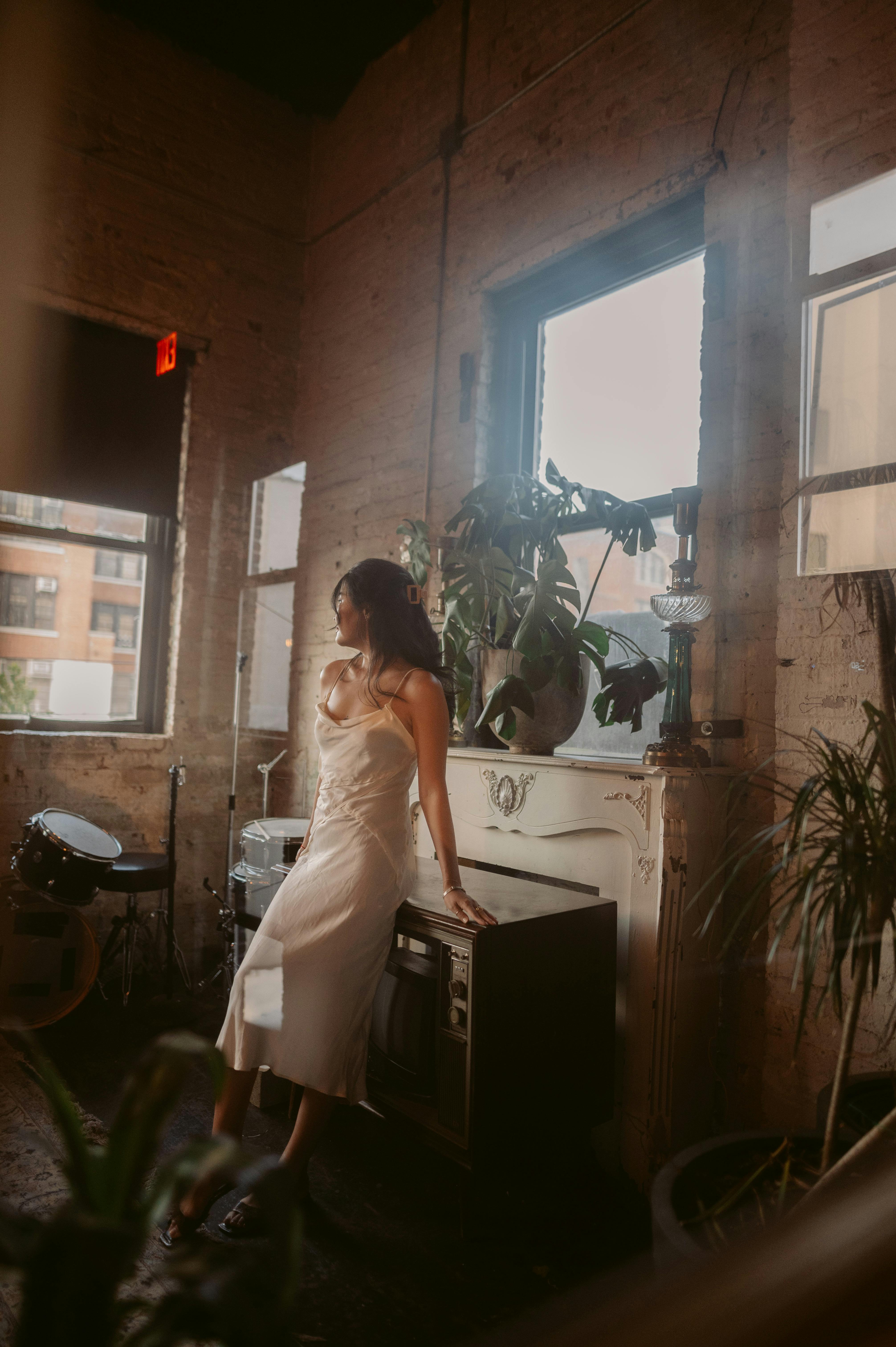 A woman in a satin nightie poses gracefully in a stylish urban apartment with vintage decor.
