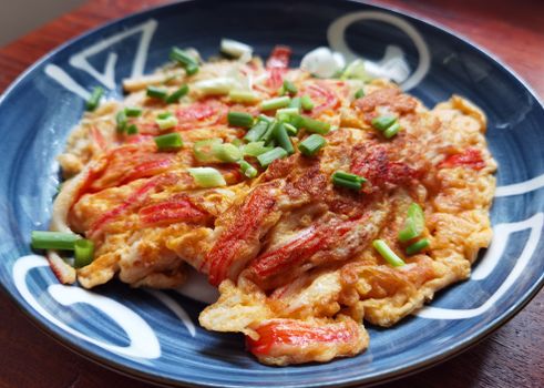 Close-up of a savory crab omelet garnished with fresh spring onions, served on a decorative ceramic plate.