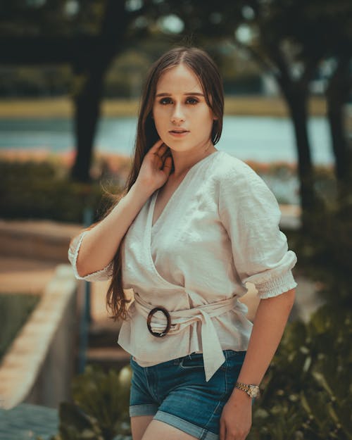 A Woman in White Shirt and Denim Shorts Looking with Her Hand on Her Neck