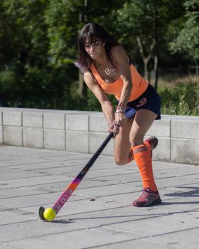 Focused female field hockey player in orange sportswear playing outdoors, demonstrating skill and agility.