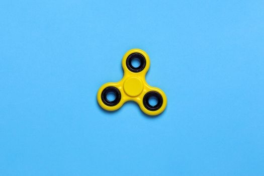 Close-up of a yellow fidget spinner on a vibrant blue background, perfect for design concepts.
