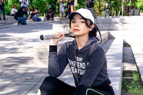 Free Confident young woman outdoors in sportswear holding a tennis racket, wearing a cap and hoodie. Stock Photo