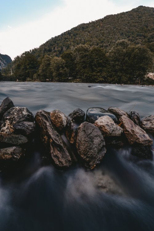 Free Peaceful river flowing through rocks with lush green hills in the background, capturing nature's tranquility. Stock Photo
