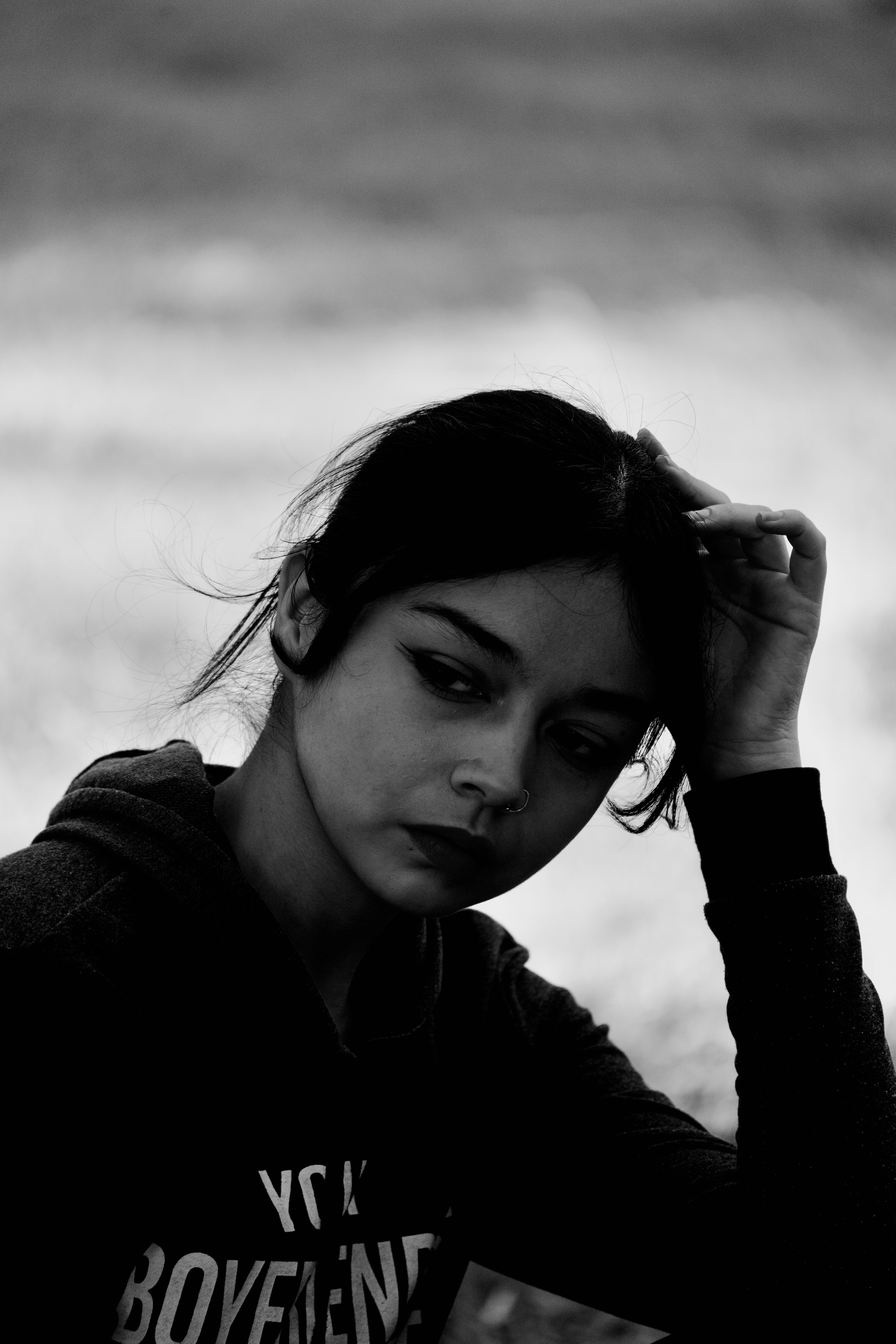 Captivating black and white portrait of a young woman wearing a nose ring, lost in thought.