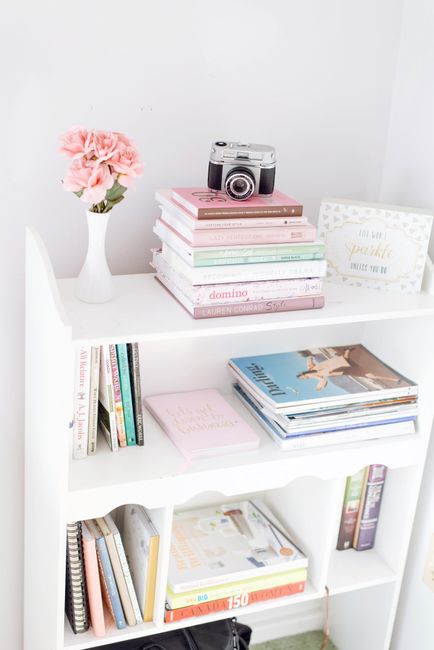 White bookshelf adorned with books, a vintage camera, and pink flowers for a chic decor look.