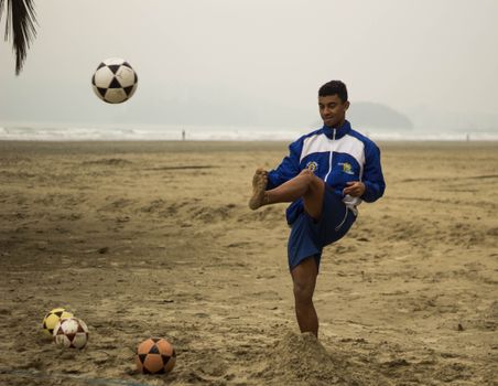 A young male athlete practices soccer on a sandy beach, showcasing skill under cloudy skies.