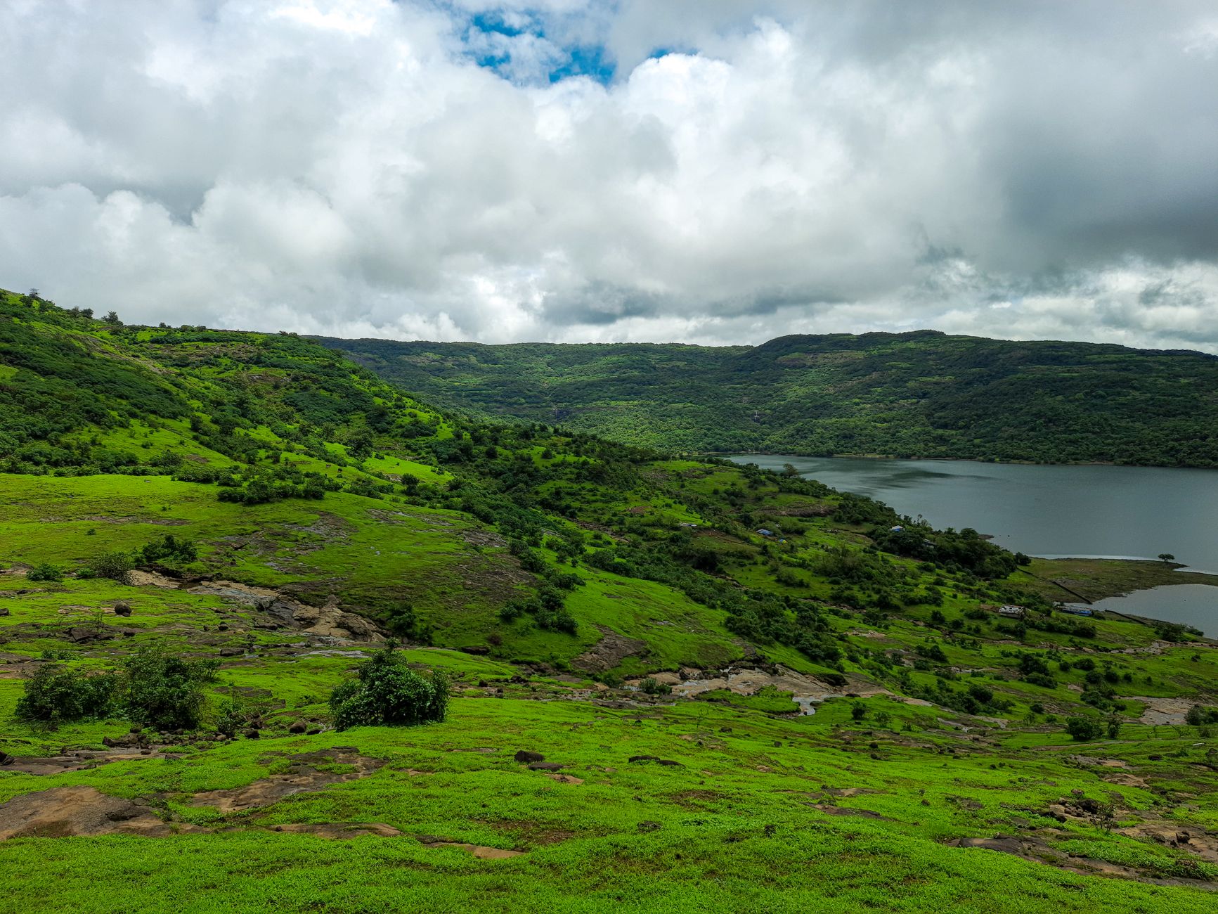 Scenic view of green hills and lake under cloudy skies in Lonavla, MH, India.