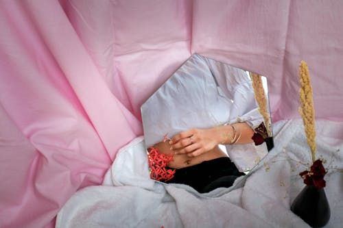 A Mirror on White Blanket with Reflection of a Person Wearing White Top