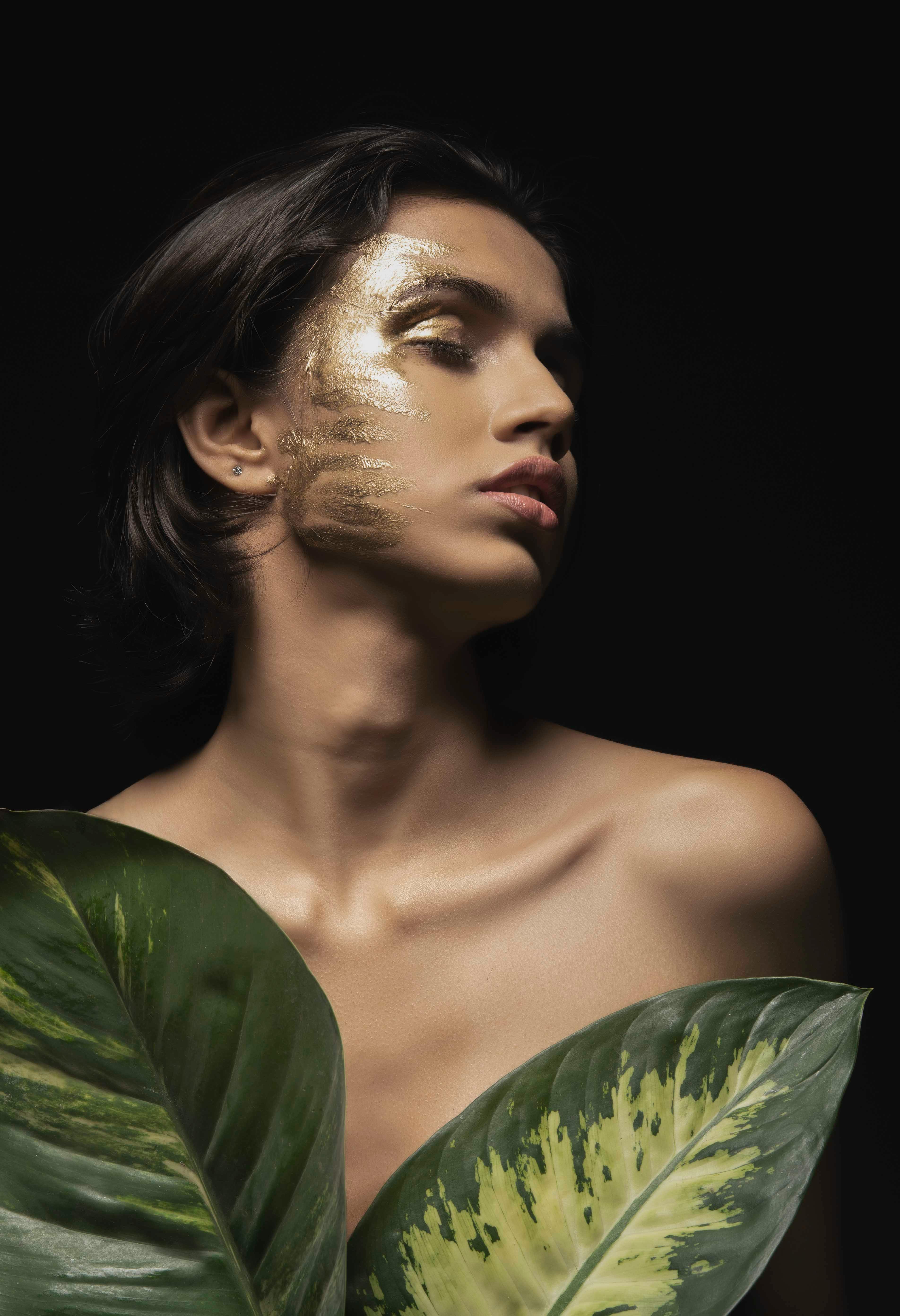 naked woman with paint on face posing with leaf