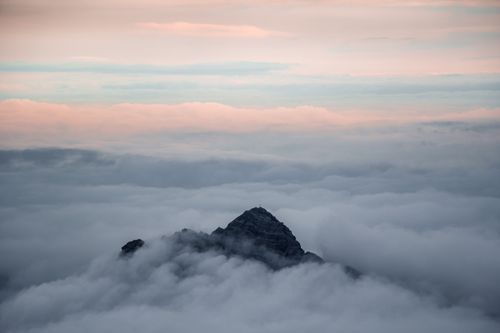 Free A breathtaking view of a mountain peak rising above a sea of clouds during sunset. Stock Photo