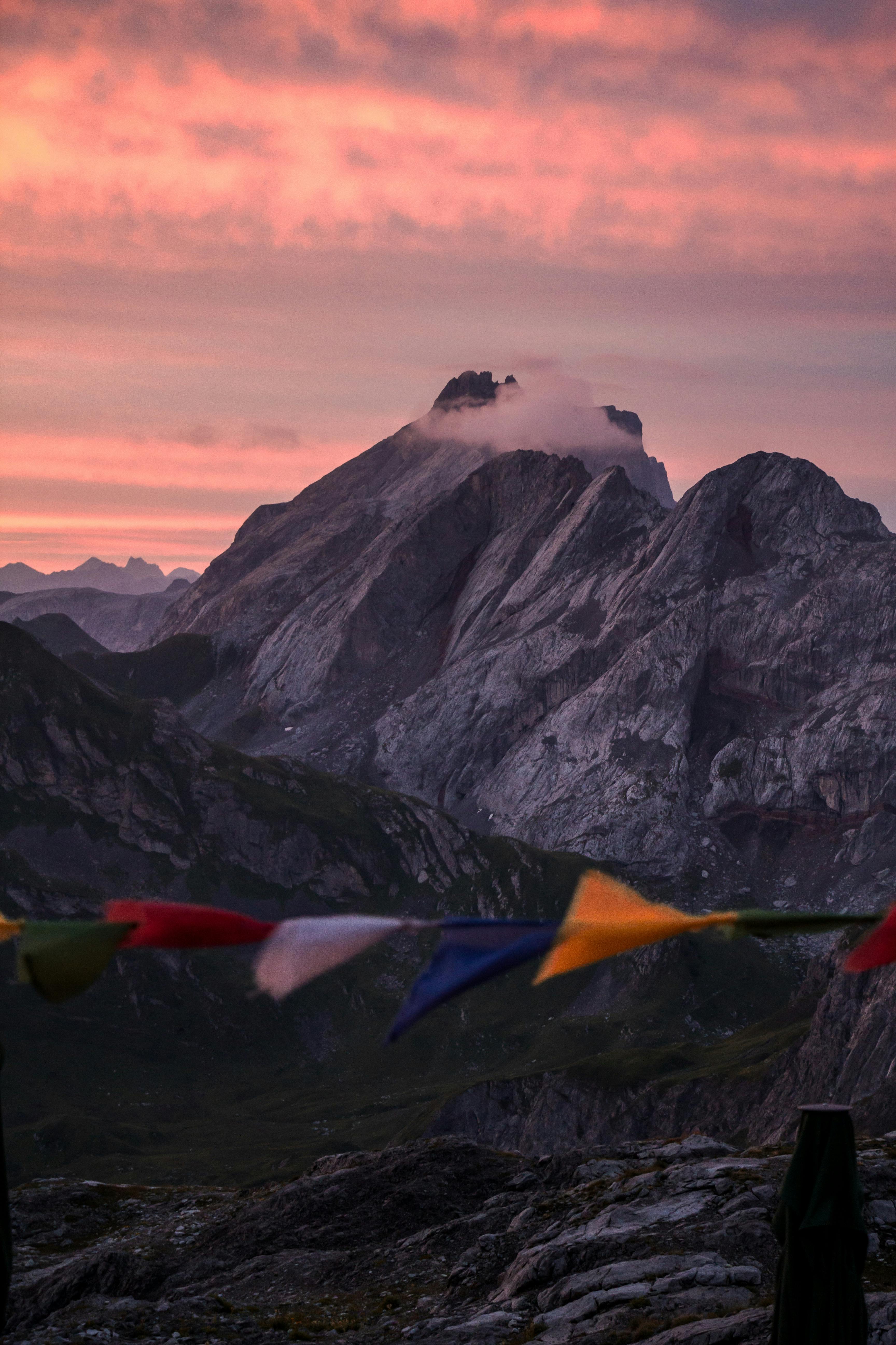 A stunning view of rocky mountains silhouetted against a vibrant sunrise sky with colorful flags in the foreground.