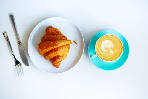 Free Tasty croissant with a latte art cappuccino on a stylish table setting, perfect for breakfast vibes. Stock Photo