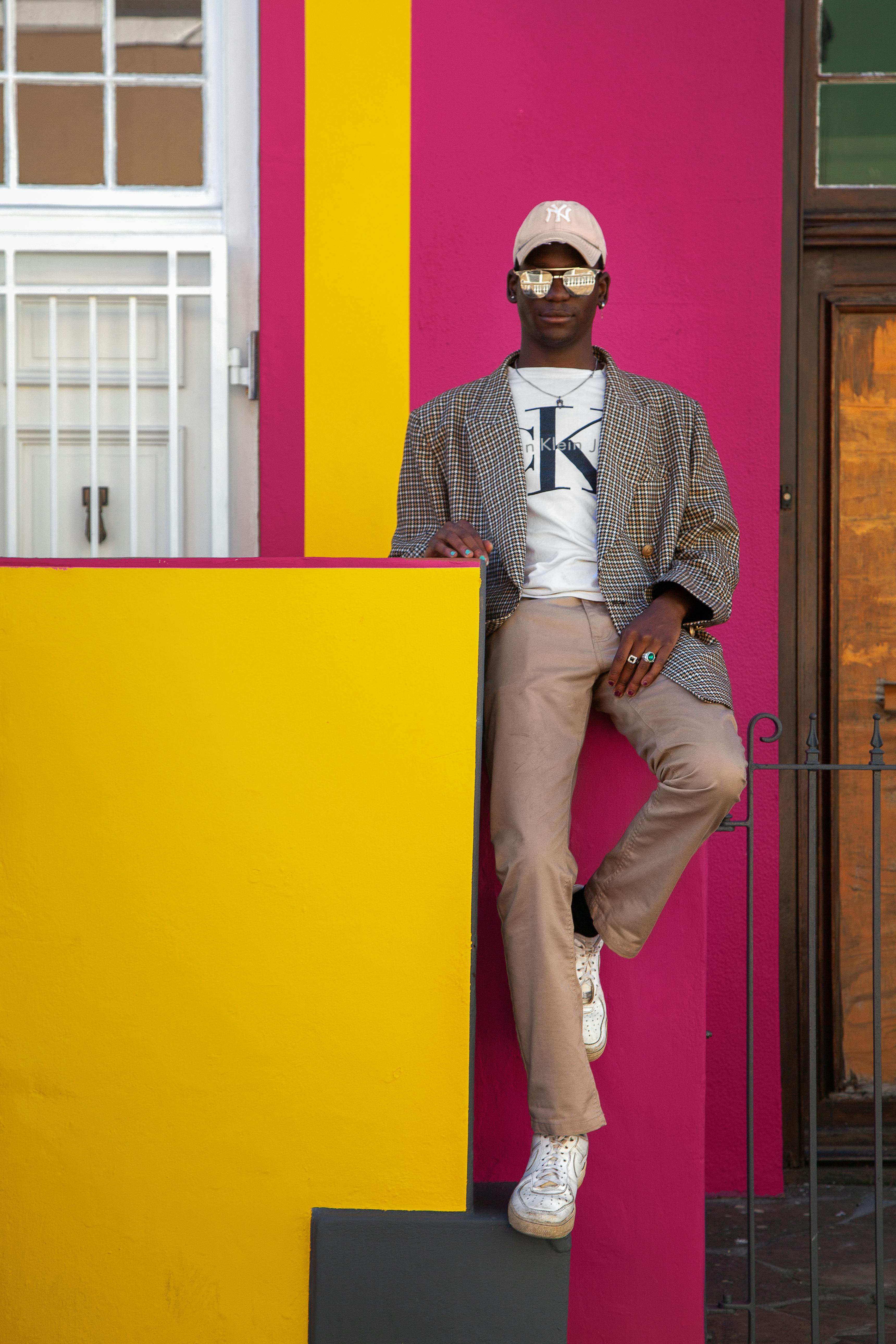 A man poses against colorful architectural backdrop in Cape Town, showcasing trendy fashion.