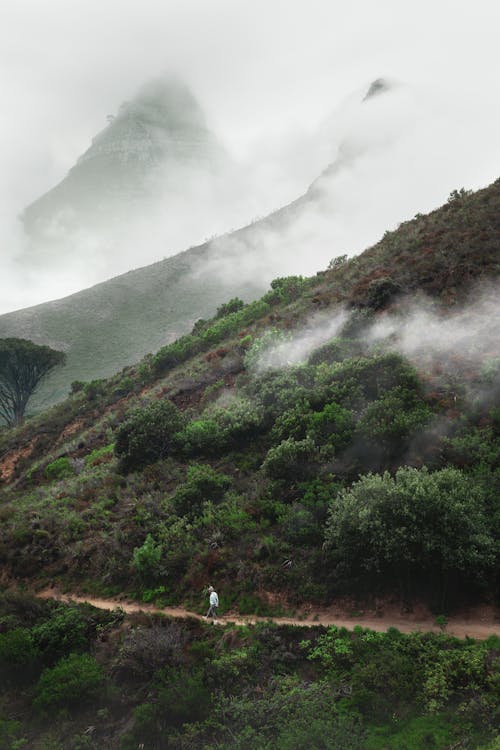 Person on Dirt Road on Hills under Clouds