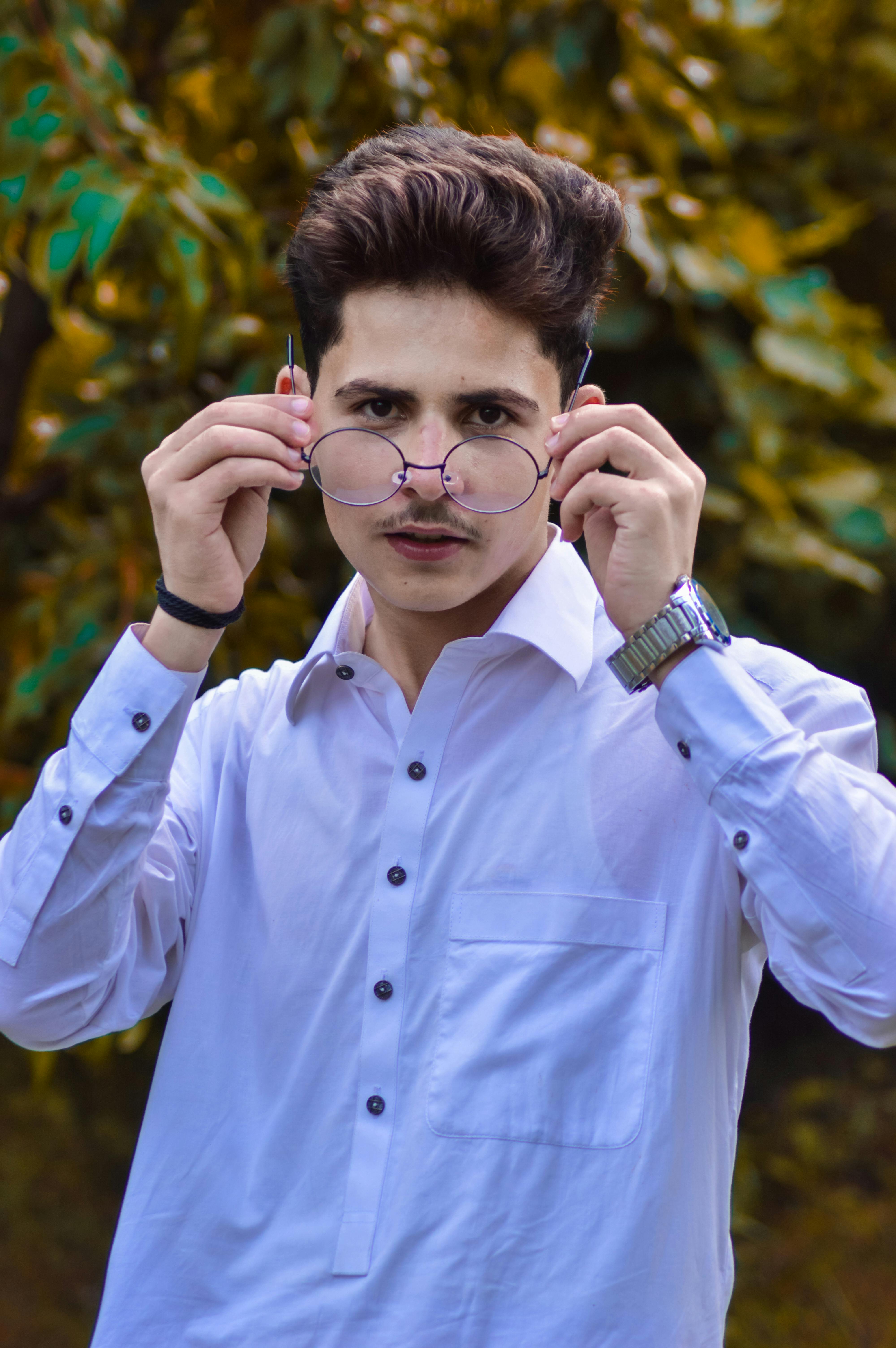 Portrait of a young man in a white shirt adjusting his glasses outdoors.