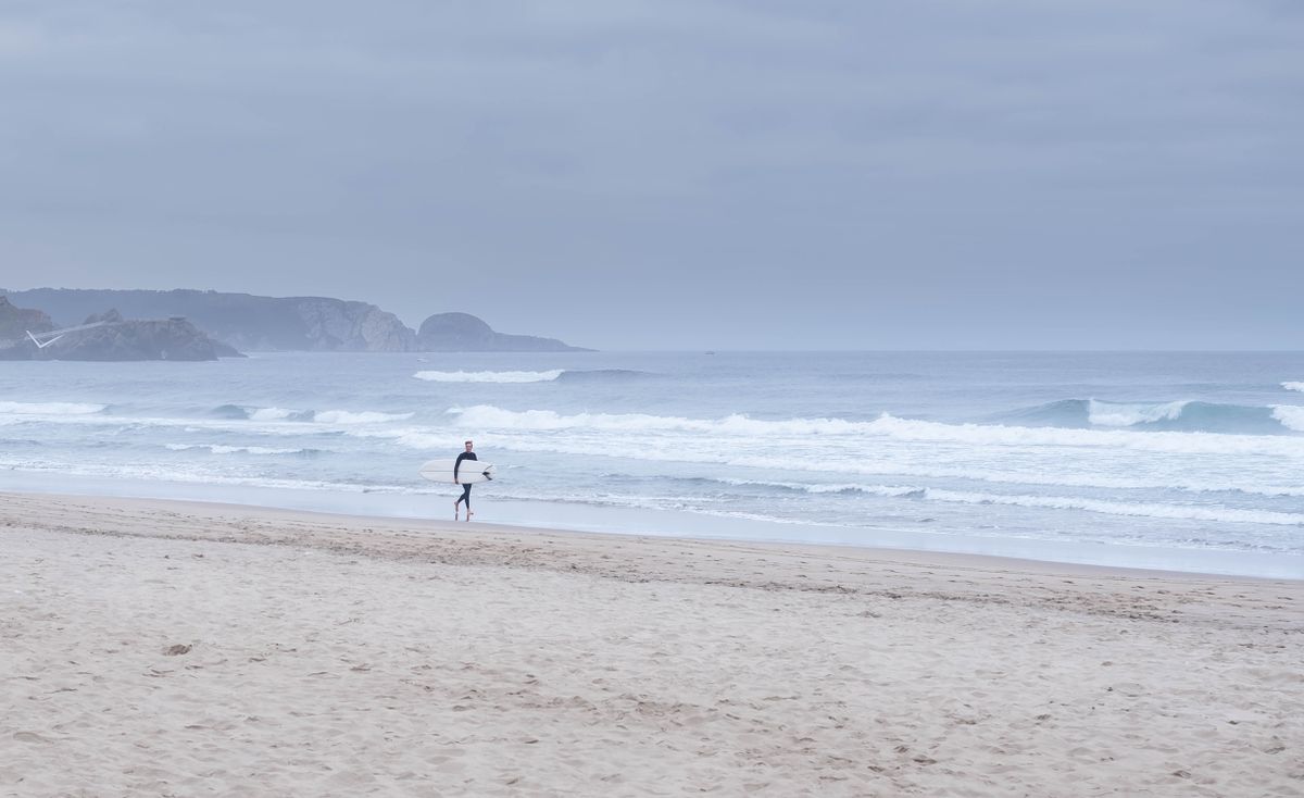 Surfer mergând pe o plajă din nordul Spaniei