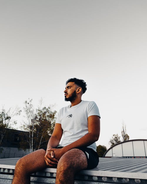 A Bearded Man in White Shirt and Black Shorts Sitting 