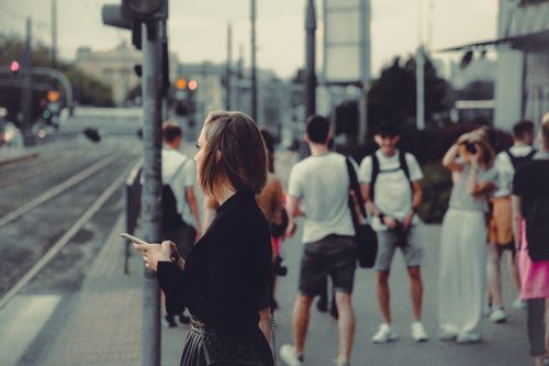 Free A stylish woman standing at a tram stop in Warsaw amidst busy city life. Stock Photo
