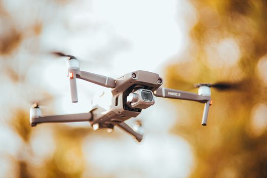 A close-up view of a drone flying in an outdoor setting with autumn colors in the background.