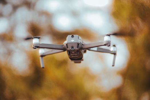 A close-up of a drone flying outdoors with blurred autumn foliage in the background.