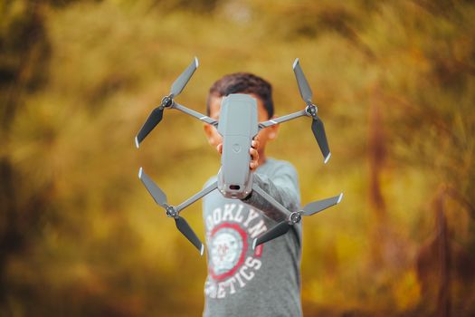 A person holding a drone in an outdoor autumn setting with blurred background.