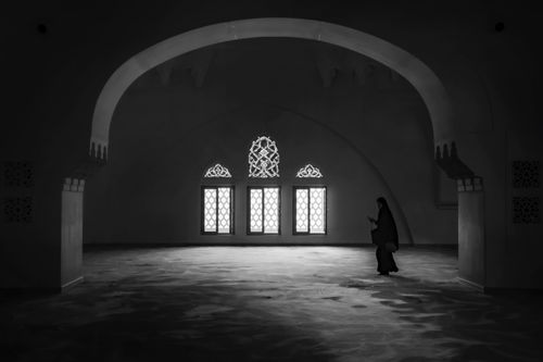 Free A peaceful black and white image of a woman in an intricately designed Islamic building with arches and windows. Stock Photo