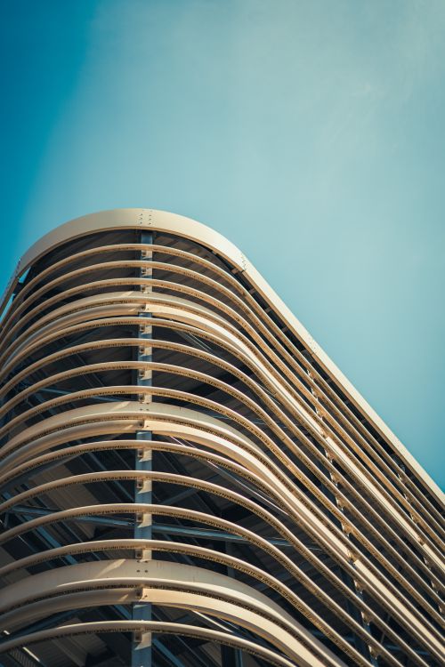 Free Dynamic low angle view of a modern building's curved facade under a clear blue sky. Stock Photo