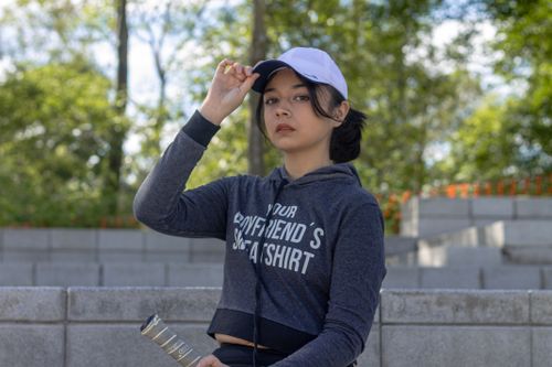 Free A young woman poses outdoors in a park, wearing a stylish hoodie and cap, with a sporty vibe. Stock Photo