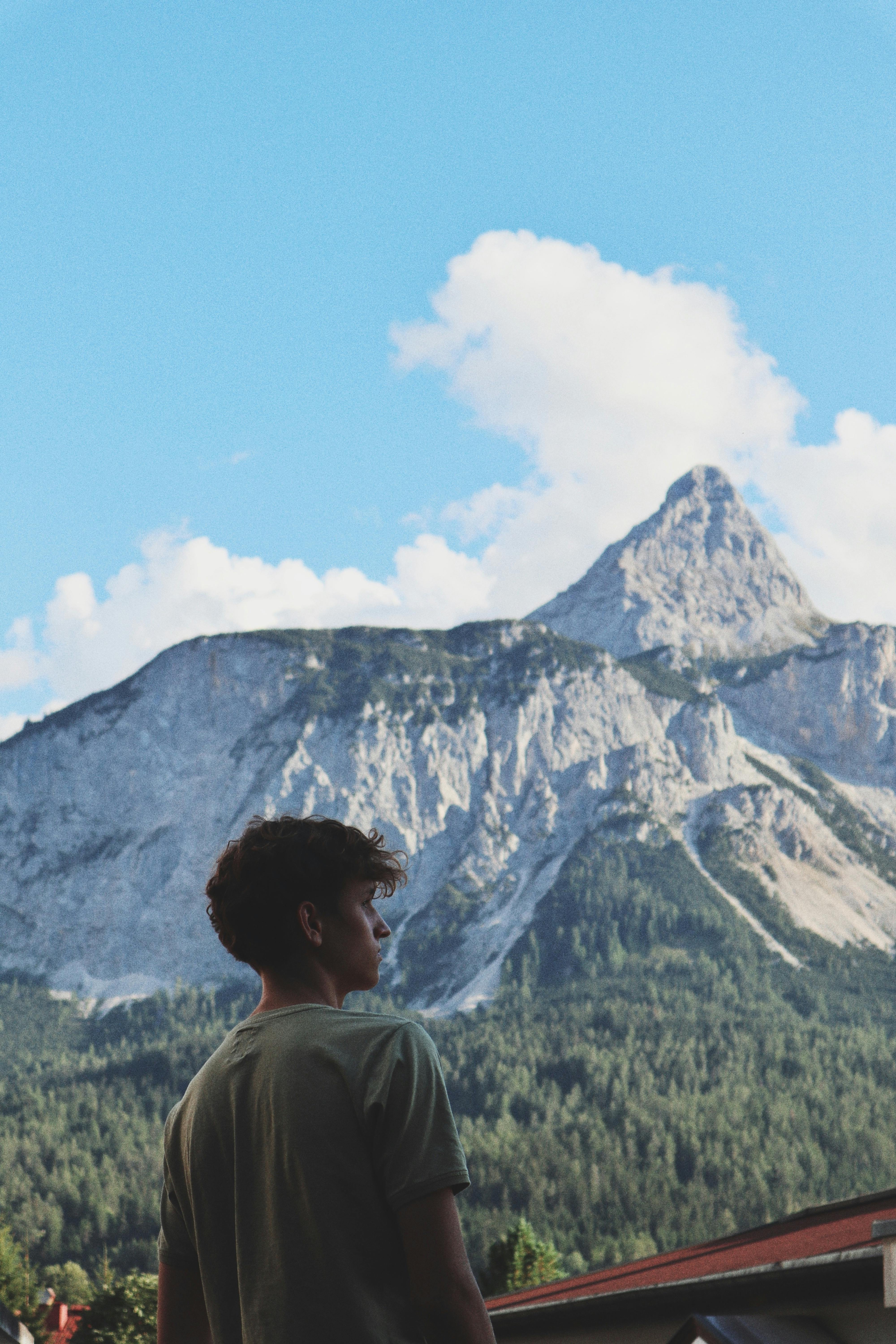 A young man in a green shirt gazes at a stunning mountain under a clear blue sky.